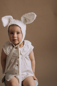 Portrait of cute baby girl sitting against wall