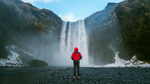 Rear view of man standing by skogafoss