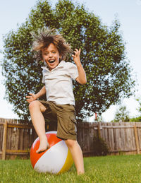 Portrait of boy enjoying while playing with ball in yard