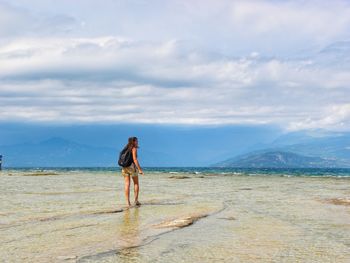 Rear view of woman standing on beach against sky