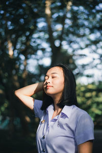 Young woman looking away while standing against trees