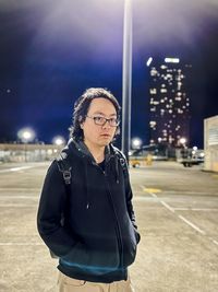 Portrait of young asian man standing against illuminated city at night.