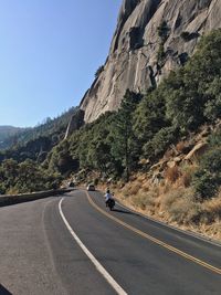 Empty road along rocky landscape against clear sky