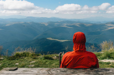 Rear view of man sitting on mountain against cloudy sky