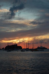 Sailboats sailing on sea against dramatic sky during sunset