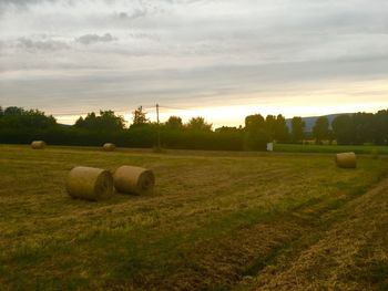 Hay bales on field against sky during sunset