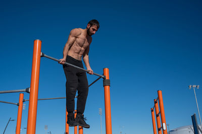 Shirtless man pulling up on horizontal bar outdoors. 