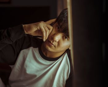 Portrait of young man sitting against wall at home