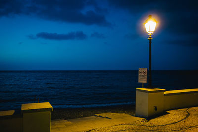 Illuminated street light by sea against sky