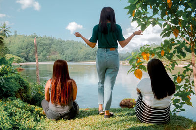 Rear view of women standing at riverbank against sky