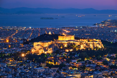 High angle view of illuminated buildings by sea against sky at dusk