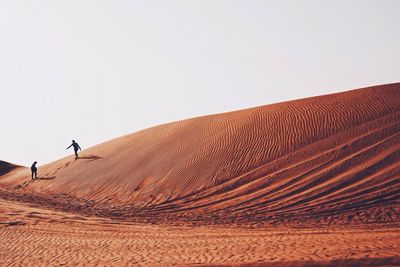 People on sand dune in dessert against clear sky