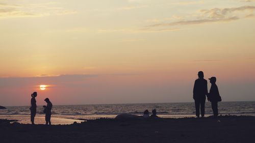 Silhouette people on beach against sky during sunset