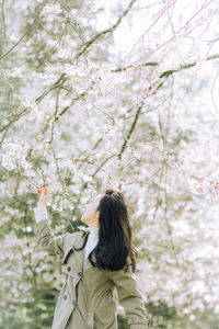 Side view of young woman standing against bare tree