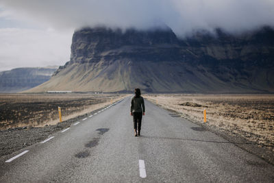 Rear view of man walking on road against mountain