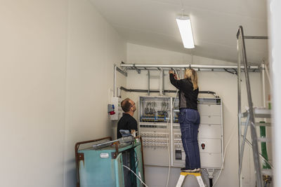 Female electrician installing cables standing by male coworker in meter room