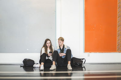 Young man sitting with female friend in corridor of university