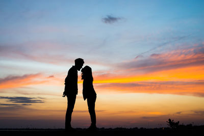 Silhouette man and woman standing against sky during sunset