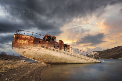 Abandoned ship on beach against sky during sunset