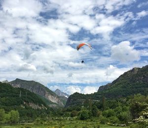 Low angle view of person paragliding over mountains against cloudy sky