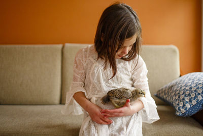 A small child sits with a small chick tenderly cradled in her arms