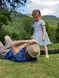 Cute girl playing with grandfather lying on grassy field