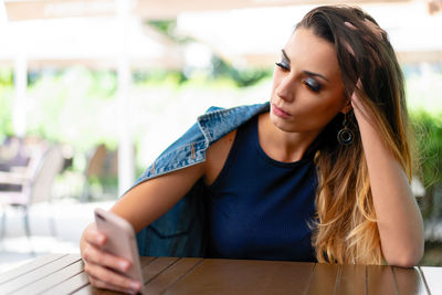 Young woman using mobile phone while sitting at sidewalk cafe