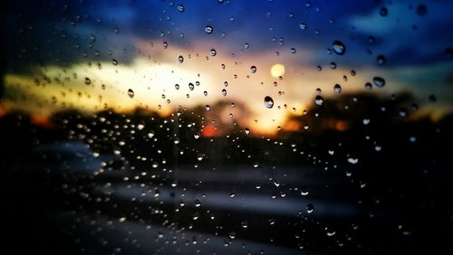Close-up of wet glass window against sky