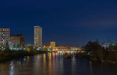 Illuminated buildings by river against sky at night