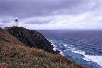 Lighthouse on cliff by sea against cloudy sky