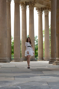 Full length of young woman standing against columns