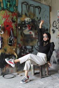 Full length portrait of woman sitting on graffiti