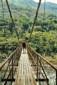 Rear view of man with backpack walking on rope bridge at tinglayan