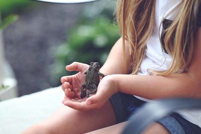 Midsection of girl holding frog while sitting in backyard