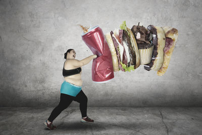 Digital composite image of woman punching fast food against wall