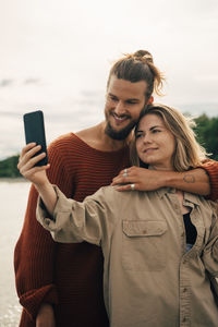 Smiling couple taking selfie on mobile phone against sky