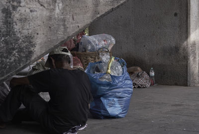 Rear view of man sitting by garbage on sidewalk