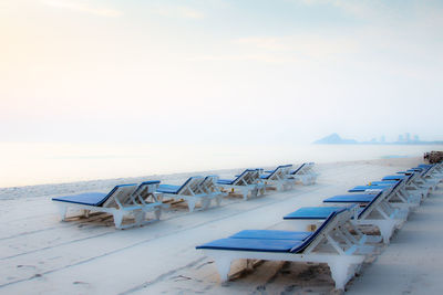 Deck chairs on beach against sky