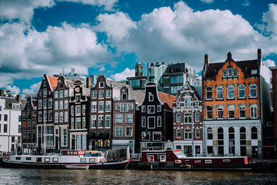 Boats on canal by buildings against cloudy sky in city