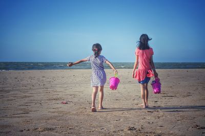 Girls walking at beach against clear blue sky