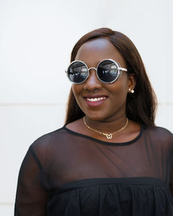 Confident young african american woman with long dark hair in black outfit and trendy sunglasses standing against white background
