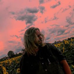 Woman standing by plants against sky during sunset