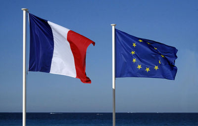 The flag of the european union and the french national flag in front of a blue sky on a sunny day