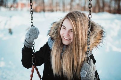 Portrait of smiling young woman on swing during winter