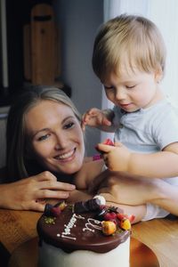 Portrait of blonde cute baby boy with mother eating cake at his birthday