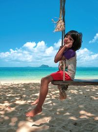 Girl sitting on swing while puckering at beach
