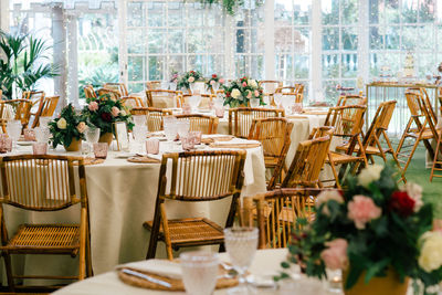 Big spacious room with festive decorated tables and wooden chairs under ceiling with green plants