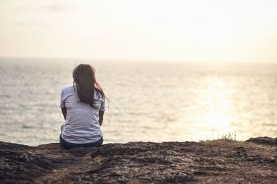 Rear view of woman sitting on sea shore against sky