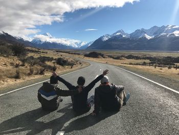 Rear view of men sitting on road against mountain range