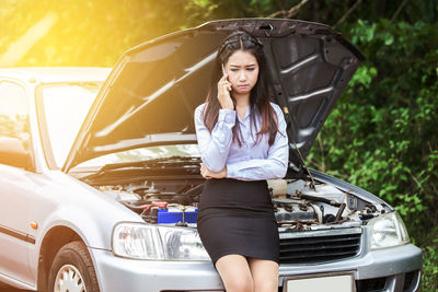 Businesswoman talking on mobile phone while standing against car